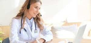 Friendly doctor working online with a laptop sitting in a desk in a consultation. orientacion-medica-telefonica